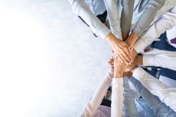 Group of diverse, business people with arms centred showing unity and teamwork.